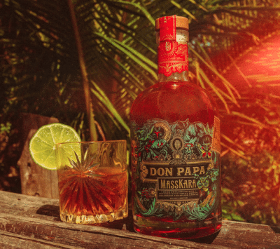 Don Papa Masskara Rumflasche neben einem Drink vor tropischen Palmen